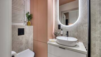 Un baño moderno con un inodoro blanco, un lavabo redondo grande y un espejo.