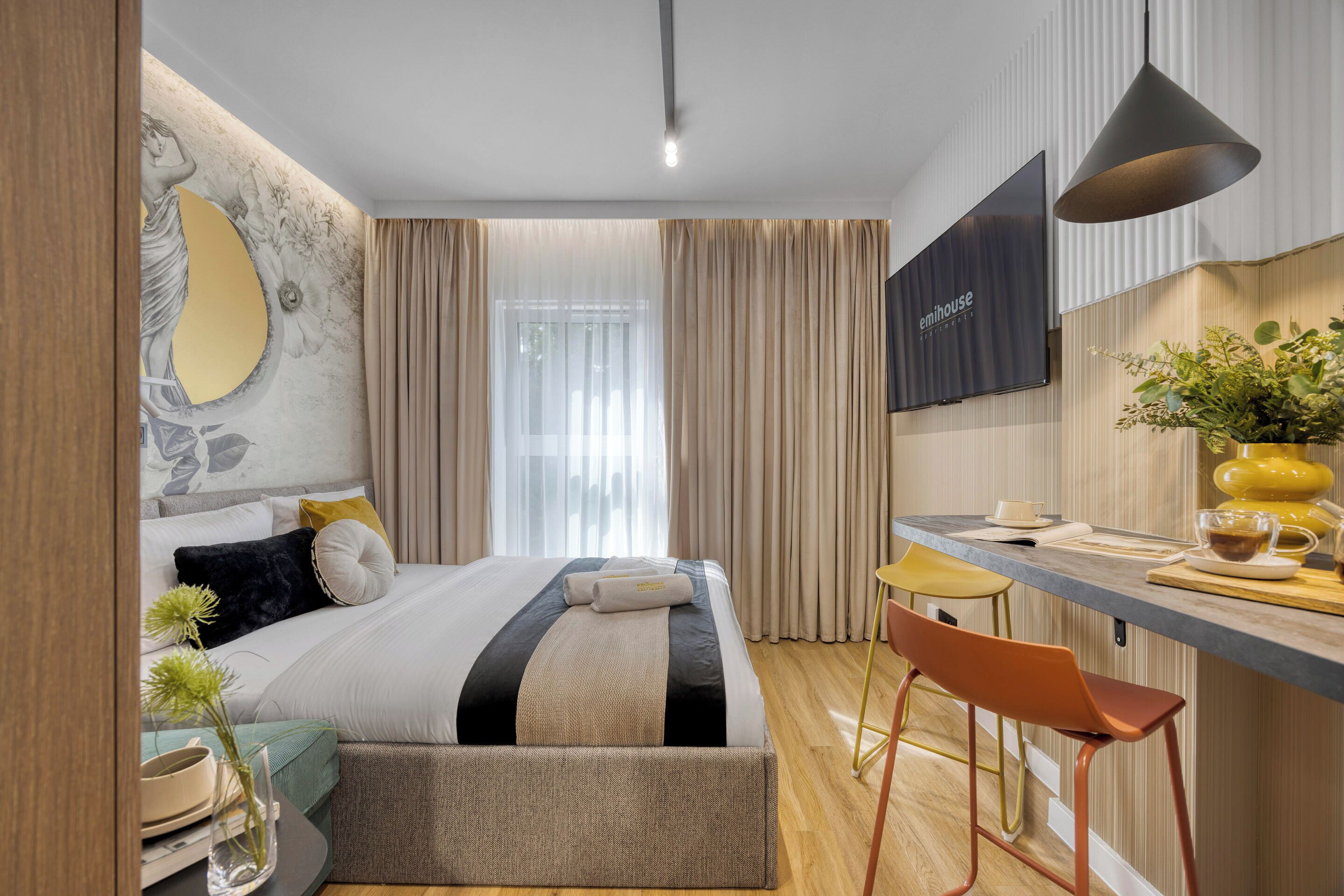 A modern hotel room with a bed, a desk, a TV, and a window with curtains.