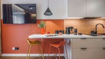 Una cocina moderna con encimera blanca, dos taburetes de bar, una lámpara colgante y el nombre de una marca visible en la pared.