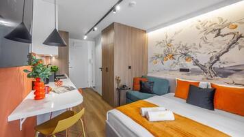 A modern hotel room with a bed, a desk, and a dining area.