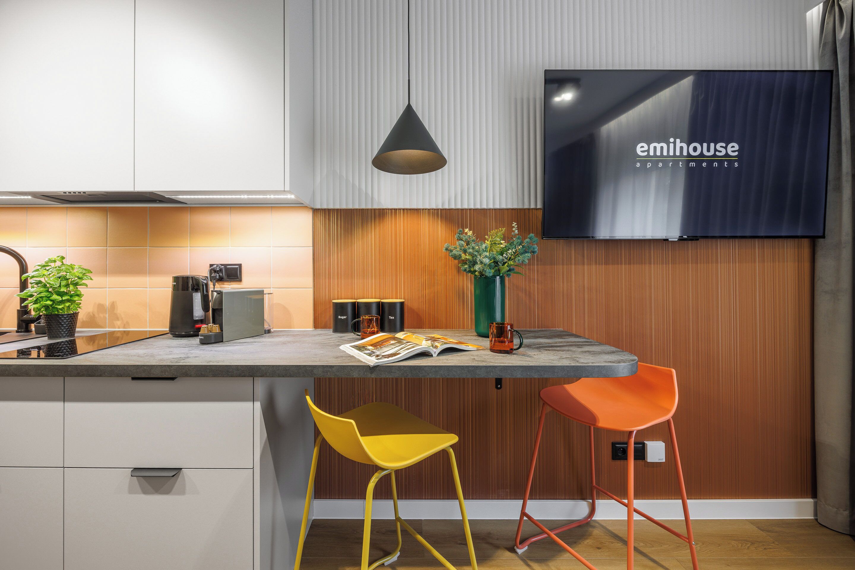 A modern kitchen with a built-in TV, wooden panel wall, and two stools.