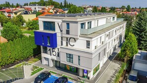 A modern building with a flat roof, solar panels, and a parking area with two cars. - Emihouse Rubikon Apartments (Rzeszów)