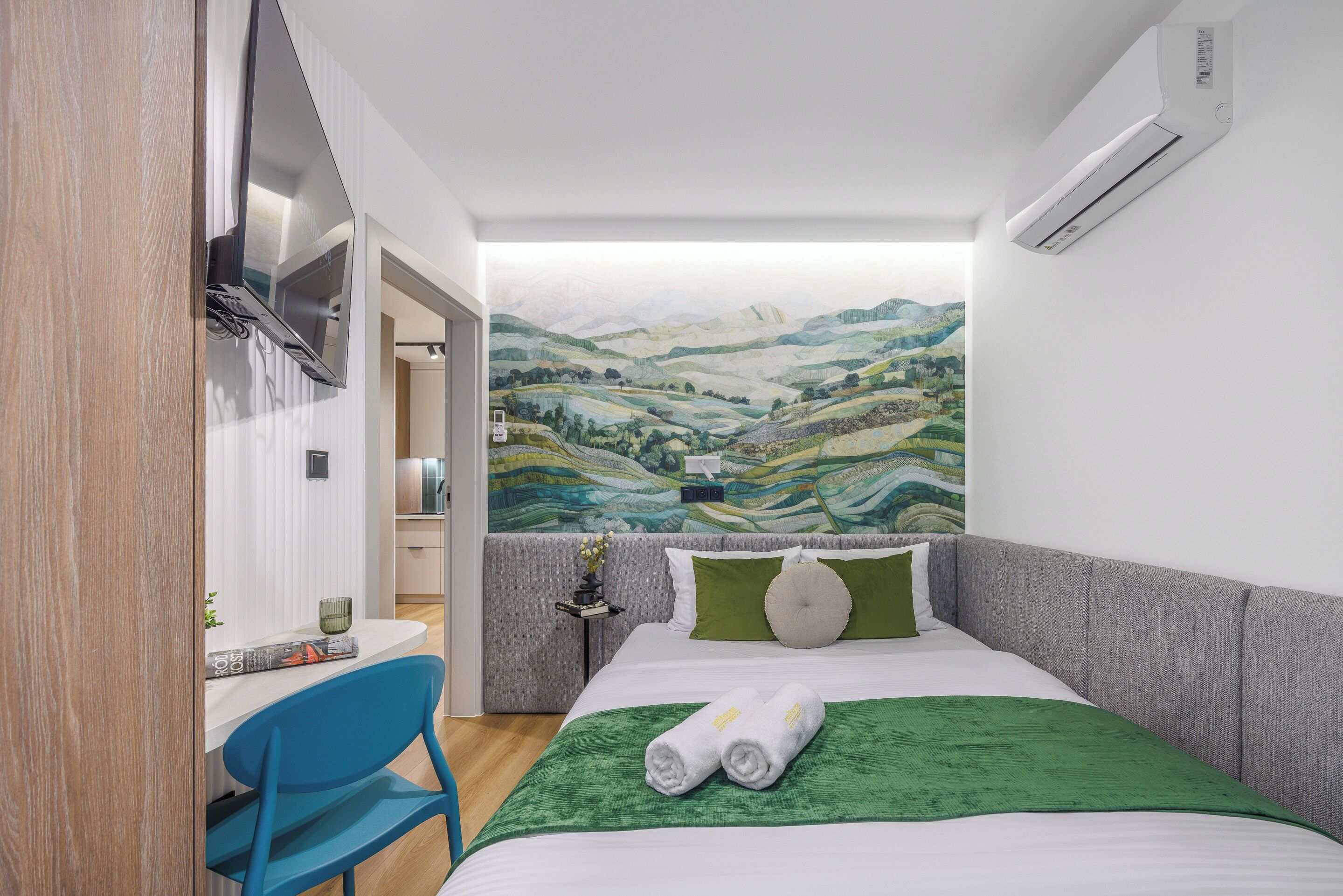 Habitación de hotel con cama, escritorio, silla y vista a colinas onduladas.