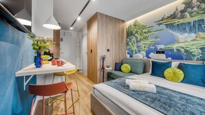 A modern hotel room with a bed, a desk, and a chair. There is a mural on the wall depicting a landscape. - Emihouse Rubikon Apartments (Rzeszów)