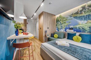 Una habitación de hotel moderna con cama, escritorio y silla. En la pared hay un mural que representa un paisaje.