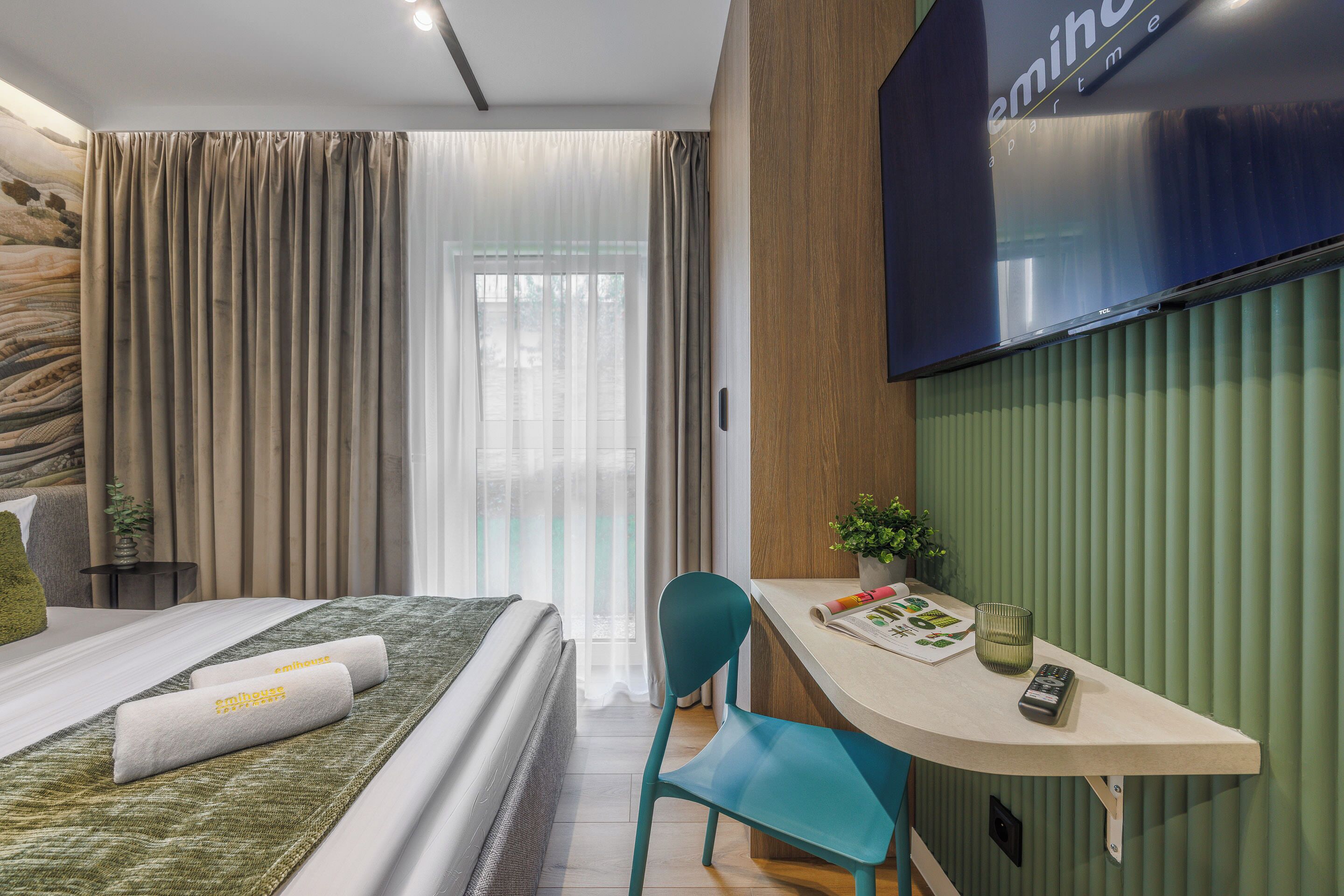 Een moderne hotelkamer met een bed, bureau, stoel, televisie en raam met gordijnen.