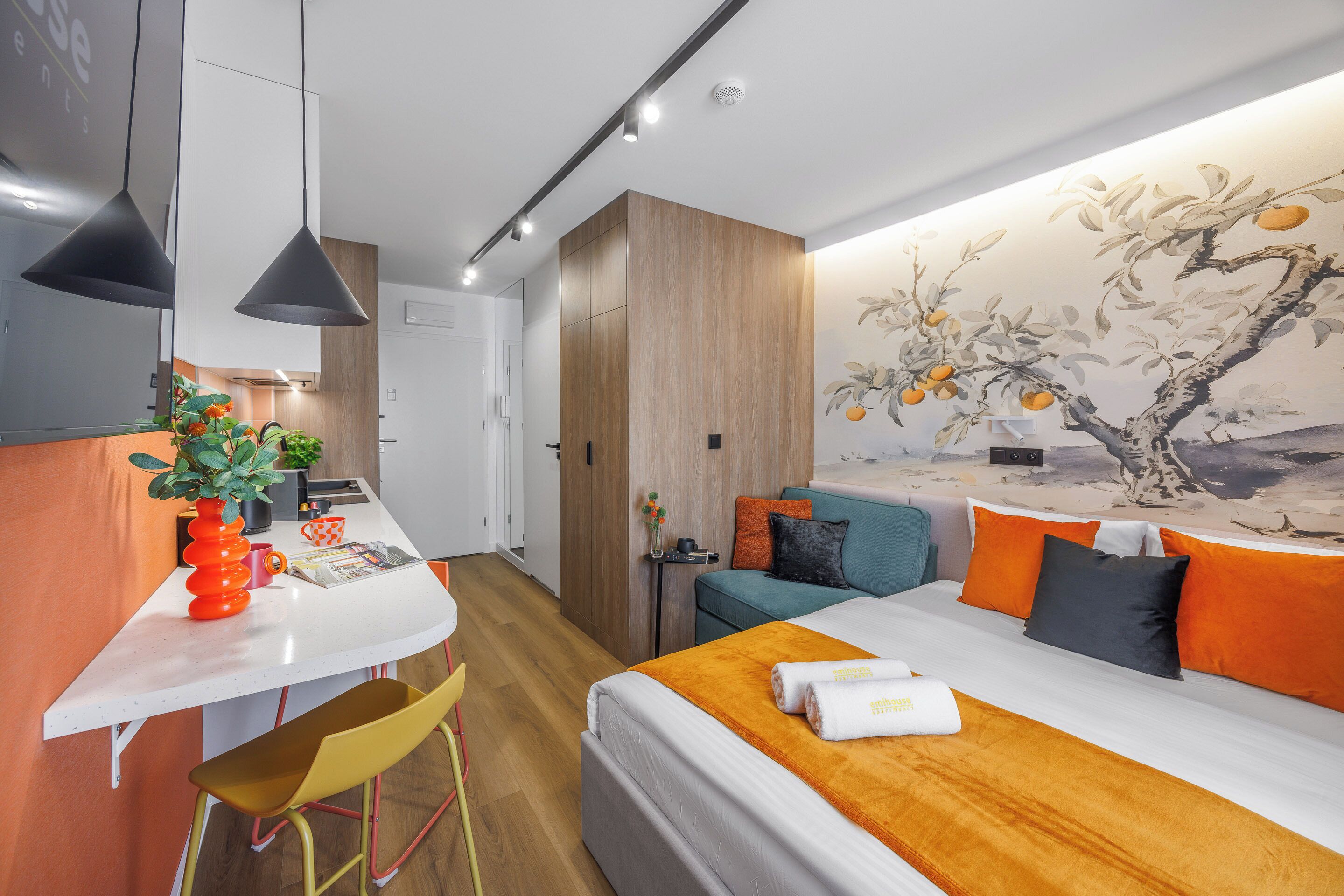 A modern hotel room with a bed, a desk, a chair, a small table, and a wall mural.