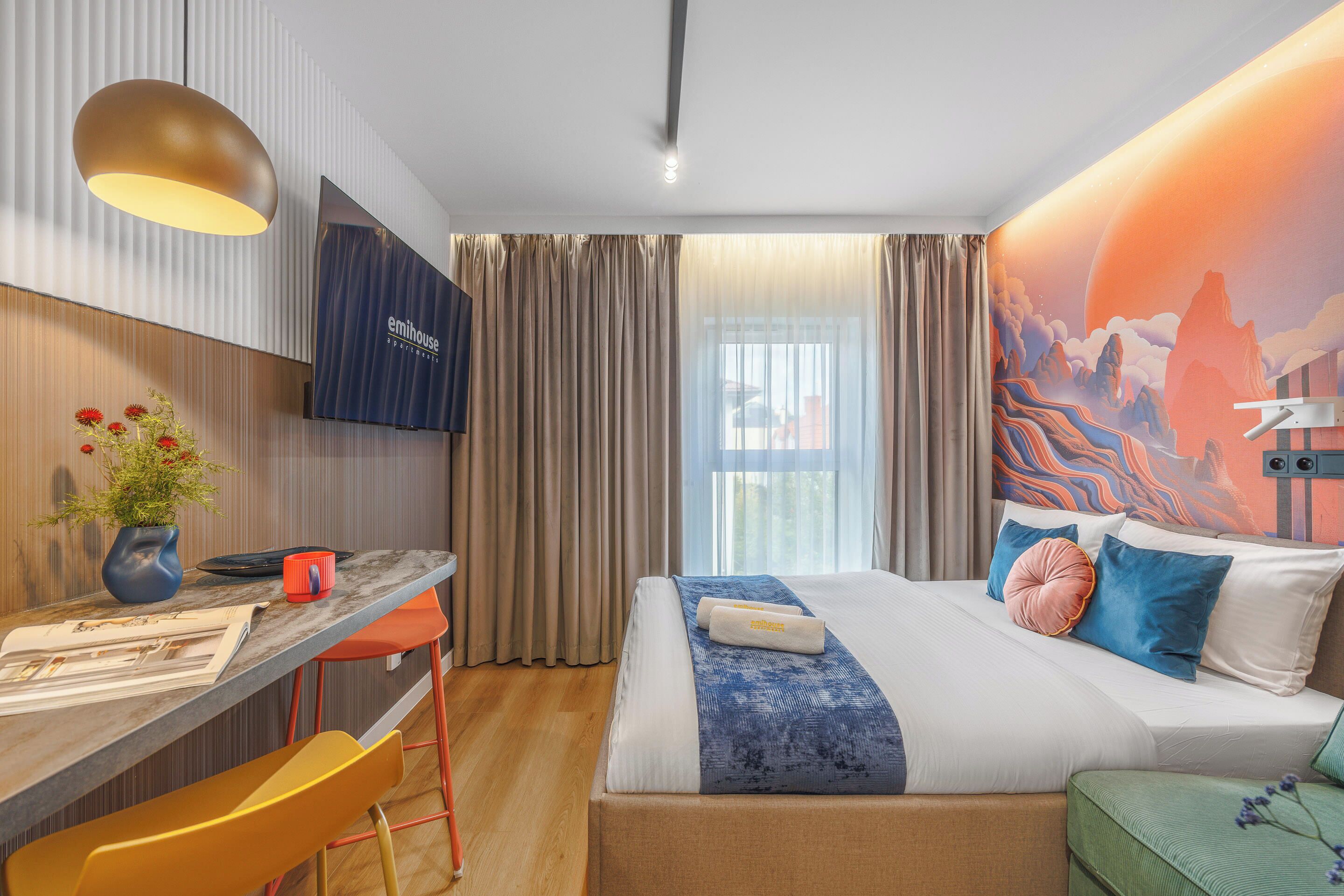 Une chambre d’hôtel avec un lit, un bureau, une chaise, une télévision et une fenêtre avec des rideaux.