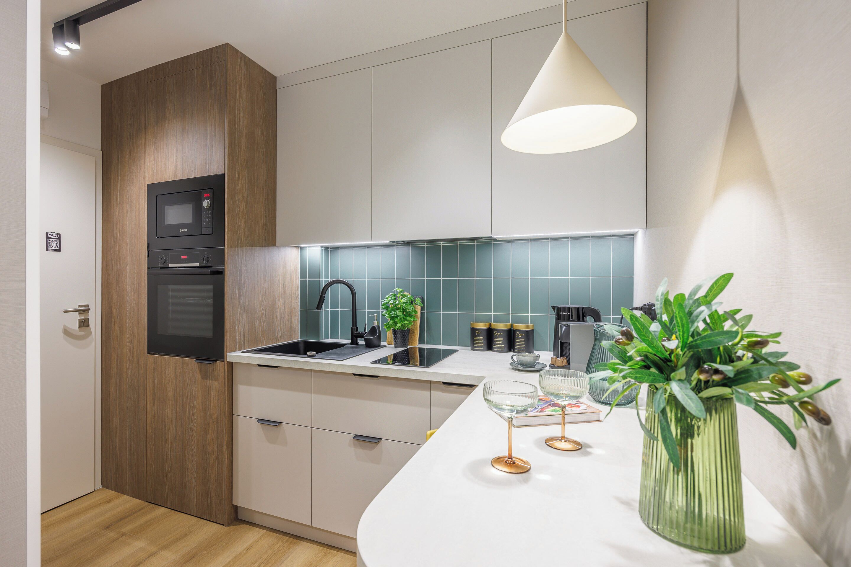 A modern kitchen with a built-in microwave, oven, and sink. There is a potted plant on the counter and a vase with greenery.