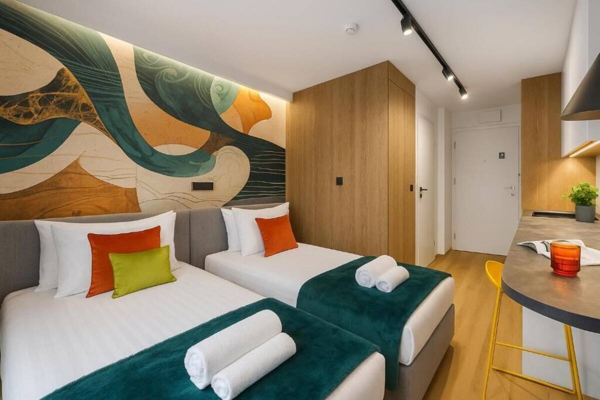 A hotel room with two beds, a wooden wardrobe, a small kitchen area, and a wall mural.