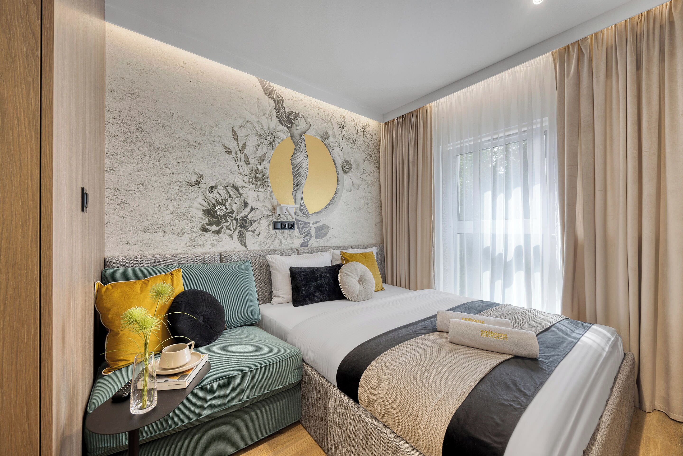 Un dormitorio con cama, sofá, espejo en la pared y ventana con cortinas.