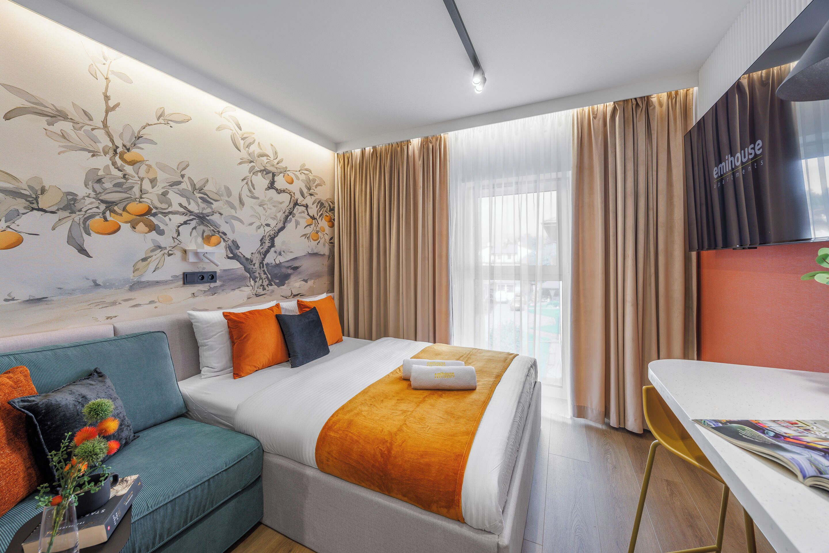 Ein Hotelzimmer mit Bett, Sofa, Tisch und Wandgemälde.