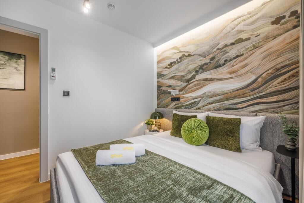 Une chambre à coucher moderne avec un grand lit, un plaid vert et une décoration murale texturée.