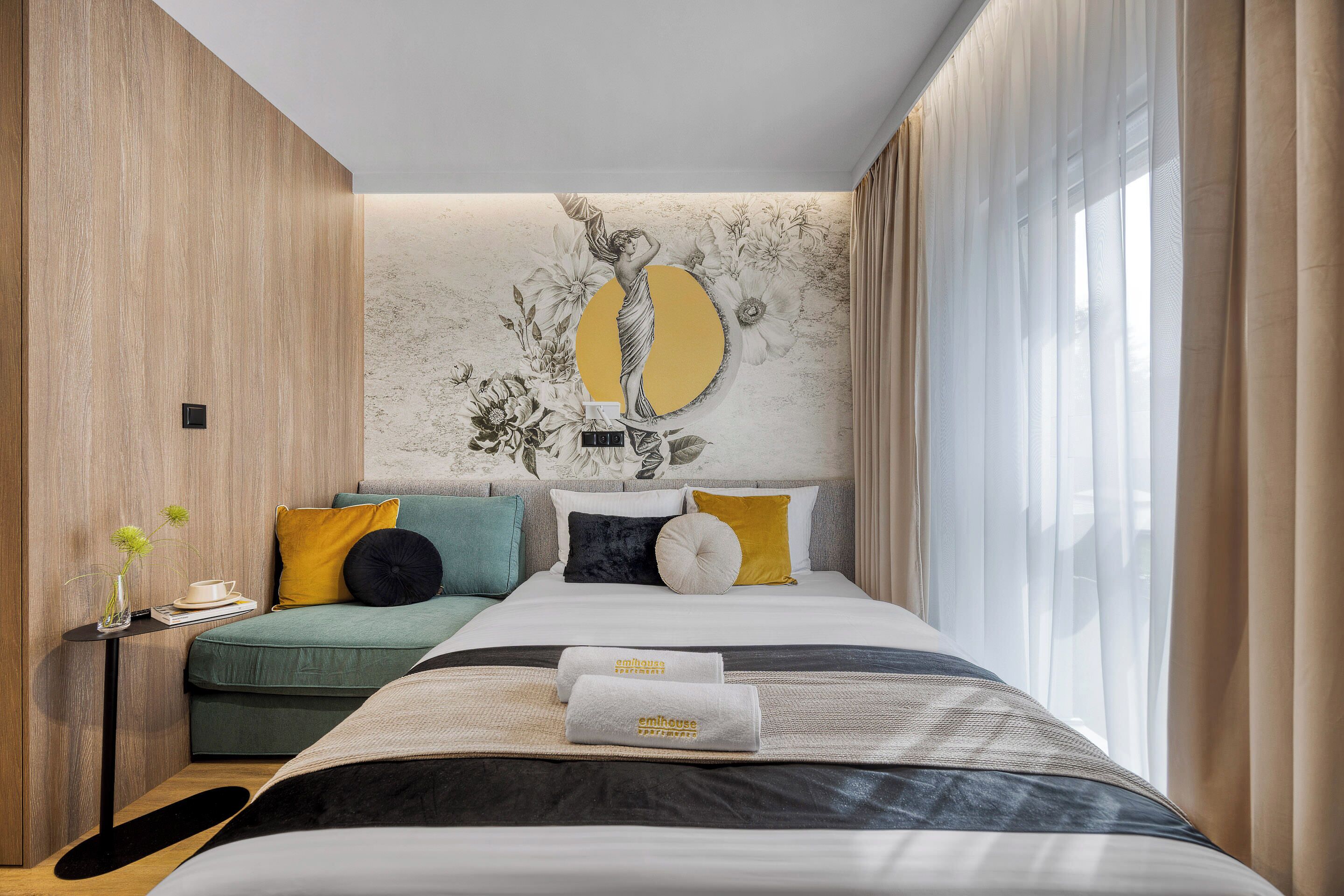 Habitación de hotel moderna con cama, una mesita auxiliar pequeña, un sofá y un ventanal con cortinas.