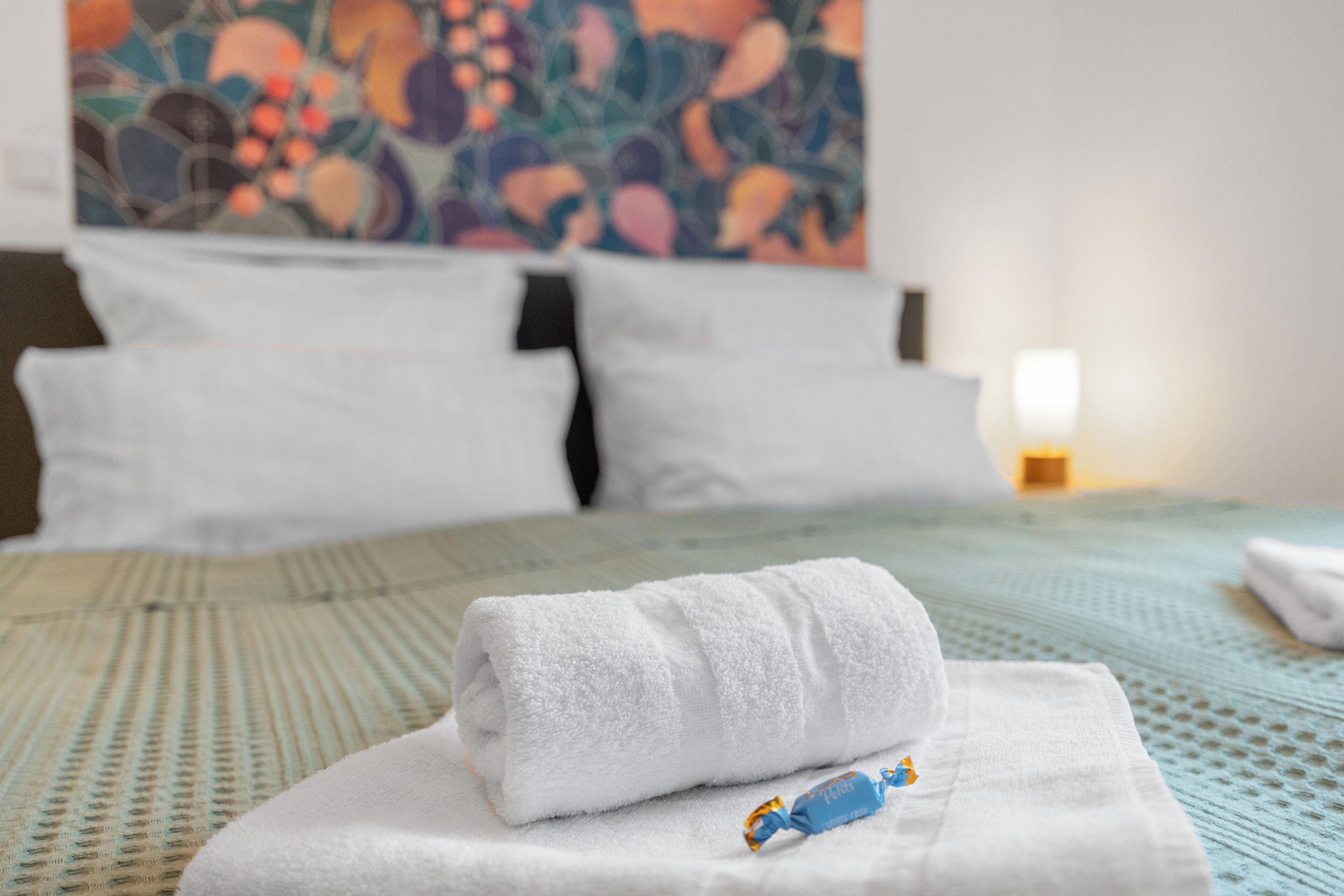 Una cama bien hecha con una toalla blanca doblada y un pequeño objeto azul encima.