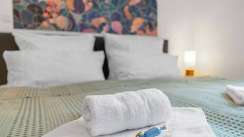 Una cama bien hecha con una toalla blanca doblada y un pequeño objeto azul encima.