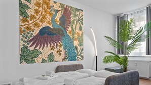 A hotel room with a bed, a large floral artwork on the wall, a potted plant, and a window with curtains. - Central | Kitchen | Netflix | 43sqm (Remscheid)