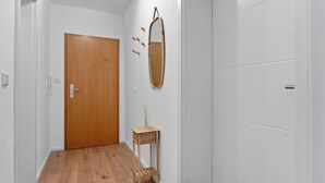 A hallway with a wooden door, a mirror, and a small wooden side table. - Central | Kitchen | Netflix | 43sqm (Remscheid)
