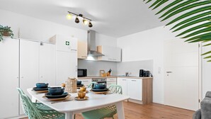 A modern kitchen with white cabinets, a white dining table with green chairs, and wooden flooring. - Central | Kitchen | Netflix | 43sqm (Remscheid)