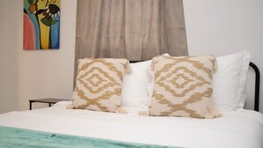 A bed with two patterned pillows, a teal throw blanket, and a painting on the wall. - Cozy Retreat | 5 mins to Beach & Downtown (Nassau)