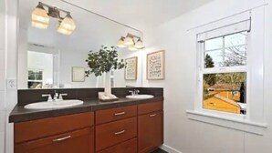 A bathroom with two sinks, a large mirror, and a window with a view of a house. - A marvelous 3-bedroom townhome in lovely Seattle  near children’s hospital (Seattle)