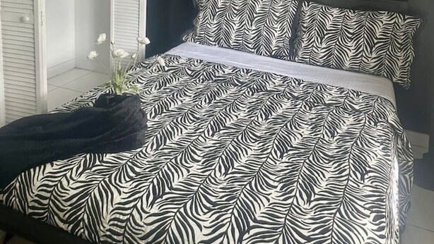 Ein Schlafzimmer mit einem Bett, das mit einem Zebra-Muster bezogen ist, einem Deckenventilator und einem weißen Kleiderschrank mit darin hängender Kleidung.