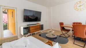 A modern hotel room with a bed, a TV, a dining table with chairs, and a clock on the wall.