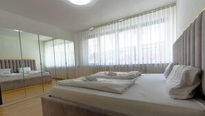 A modern bedroom with a large bed, a sofa, a mirror, and sheer curtains.