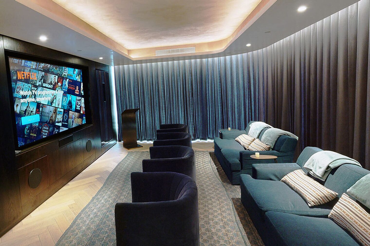 A modern home theater with a large flat-screen TV, dark blue seating, and a patterned rug.