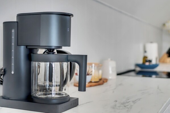 Une machine à café moderne, dotée d’une verseuse transparente et d’un écran numérique, est posée sur un plan de travail en marbre dans une cuisine.