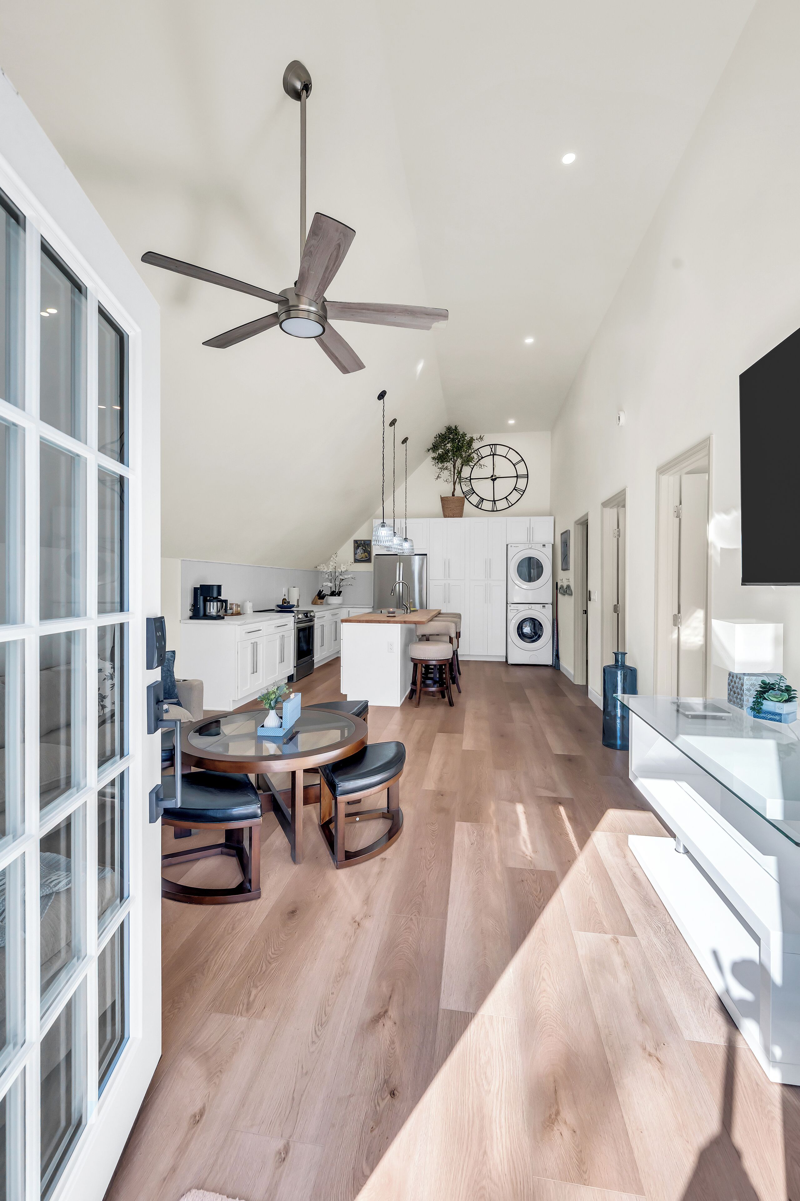 A modern kitchen with a ceiling fan, a dining area with a round table, and a large window.