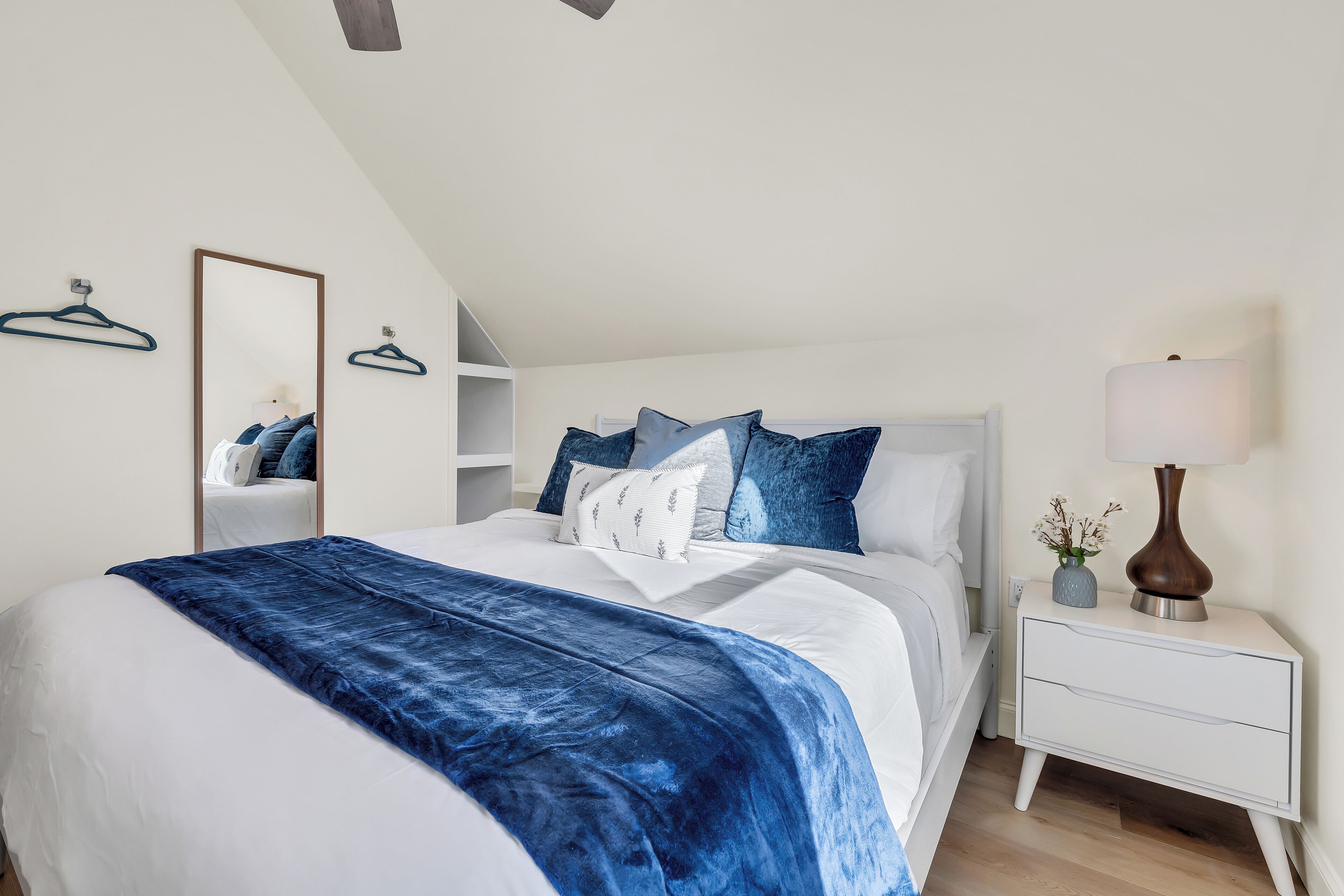 Une chambre à coucher bien rangée, avec un grand lit, une table de chevet avec une lampe et un miroir au mur.