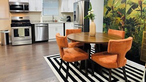 A modern kitchen with white cabinets, stainless steel appliances, a dining area with orange chairs, and a tropical mural. - Getaway in Greater Navy Yard - 4BR/3BA -Sleeps 10+ (Washington)