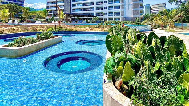Et moderne hotel med en tagpool, omgivet af frodig vegetation og høje bygninger.