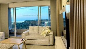 En moderne stue med en sofa, et sofabord og et fjernsyn. Der er en balkon med udsigt over byen og en byggekran.