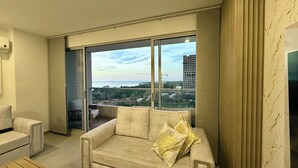En moderne stue med sofa og lænestol, samt en skydedør til en balkon med udsigt over byen.
