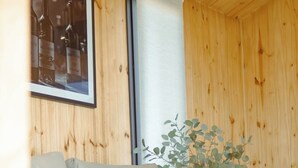 Una habitación con paneles de madera, un sofá gris, una mesita y un cuadro con botellas de vino.