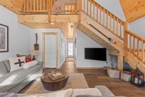 Amplia sala de estar con una escalera de madera, un sofá con cojines, una mesa de centro y un televisor de pantalla plana.
