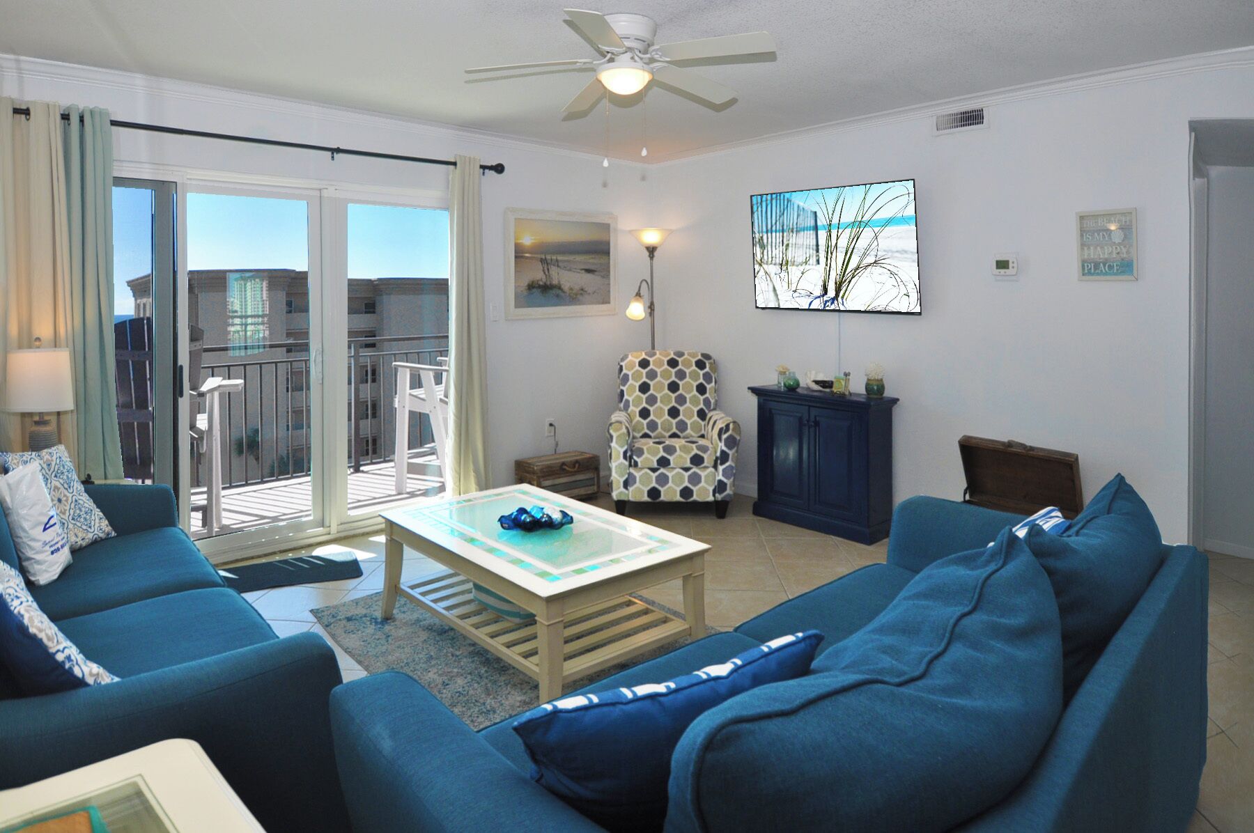 Ein Wohnzimmer mit blauem Sofa, einem gemusterten Sessel, einem Couchtisch und Blick auf den Balkon.