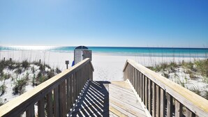 Ein hölzerner Steg führt zu einem Strand unter blauem Himmel.