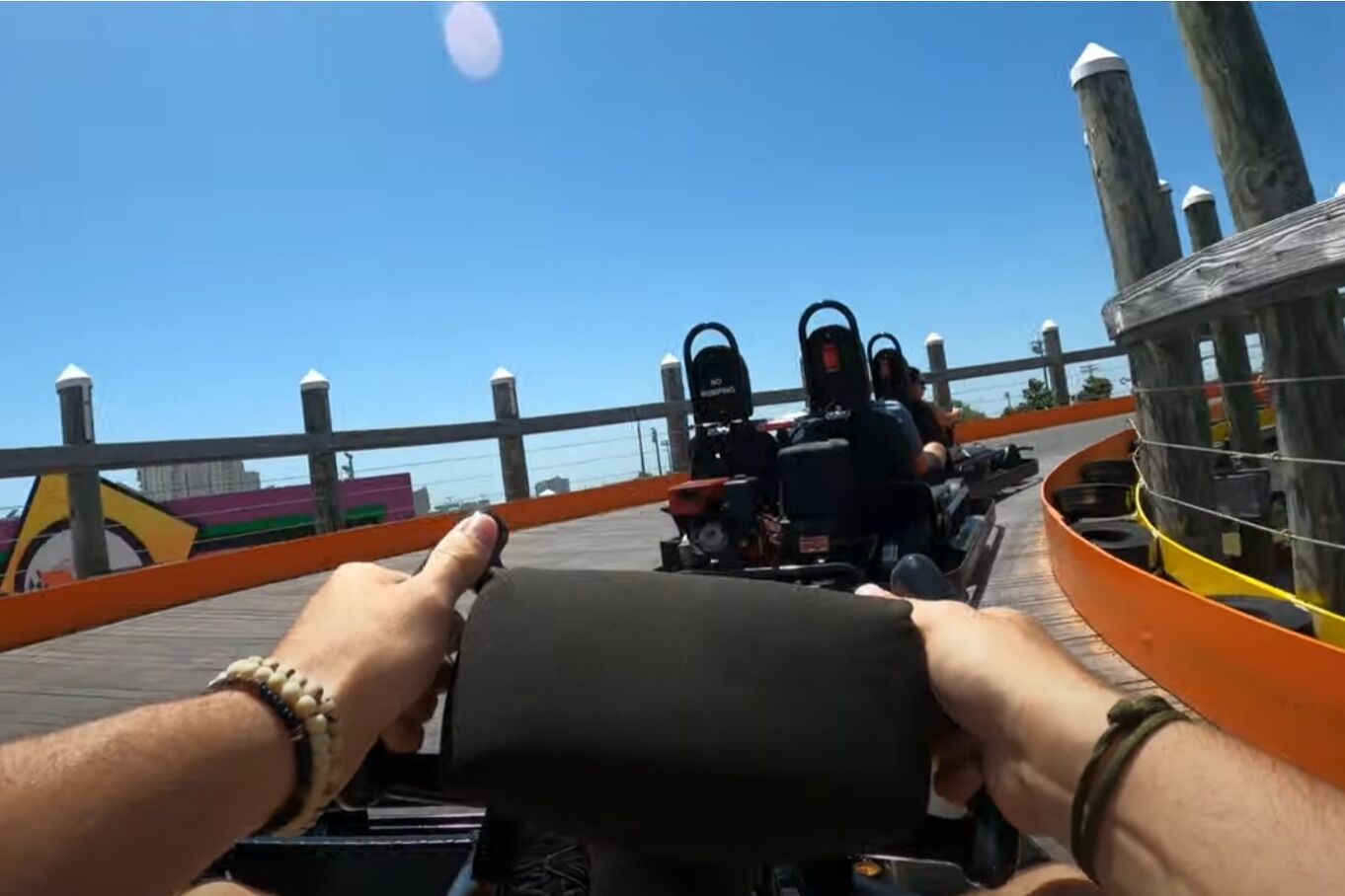 Une personne conduit un kart sur une piste en bois, avec un ciel bleu dégagé en arrière-plan.