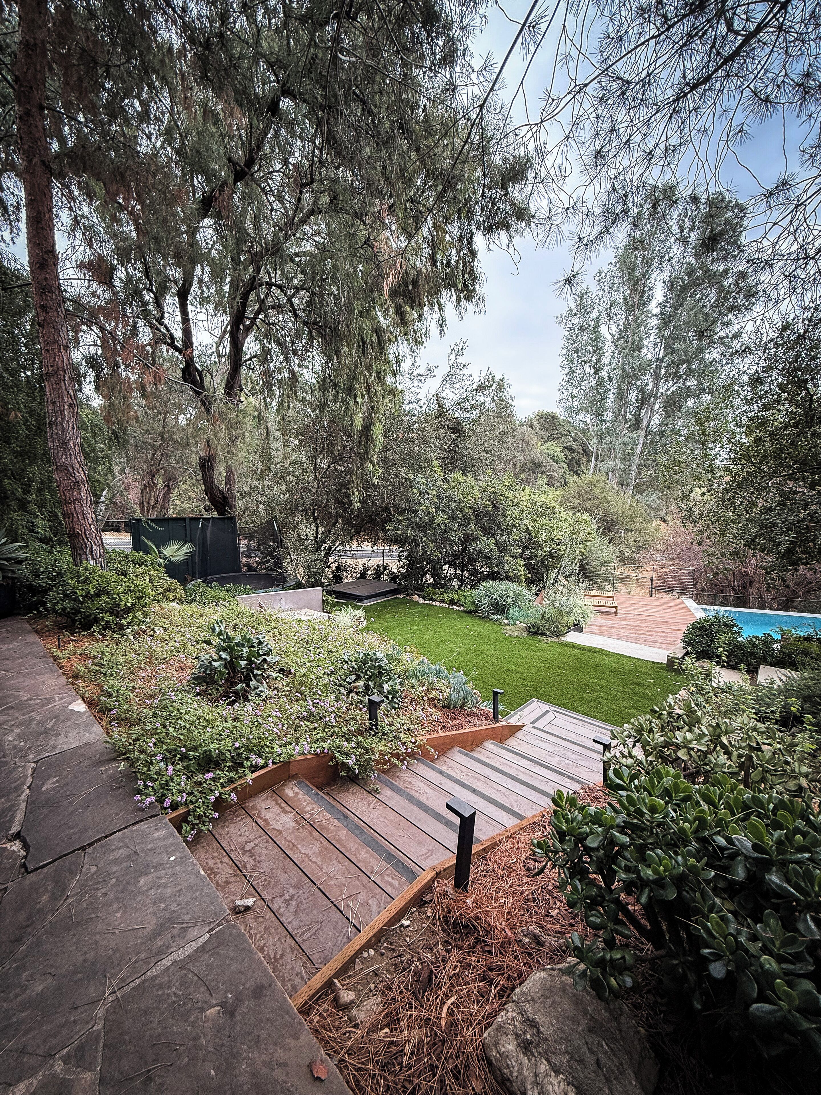 A landscaped backyard with a wooden deck, a small pool, and various plants.