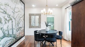 Ein Essbereich mit rundem Tisch, schwarzen Stühlen, einer Chandelierleuchtre und einem großen abstrakten Gemälde an der Wand.