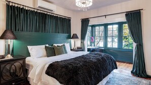 Ein Schlafzimmer mit einem großen Bett, zwei Nachttischen, einer Kristallleuchter und Blick ins Freie durch ein Fenster mit Vorhängen.
