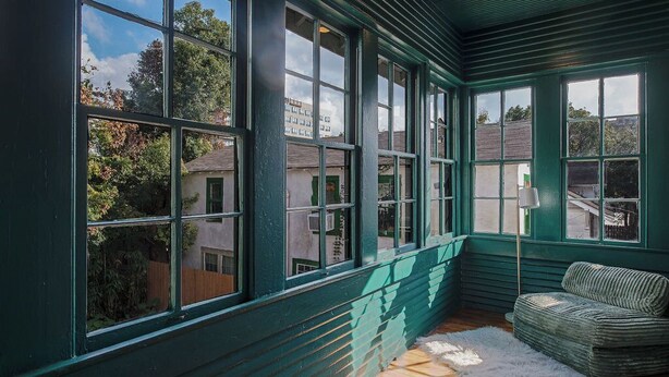 Ein Zimmer mit großen Fenstern, einem grün gestrichenen Außenbau und einem weißen Teppich.