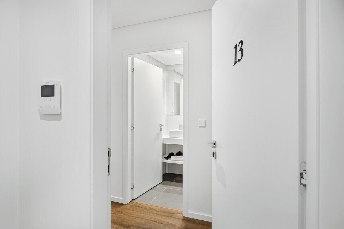 Een gang met witte wanden, een houten vloer, een deur met het nummer 13 en een beveiligingscamera.