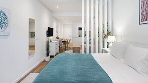 Ein modernes Hotelzimmer mit einem Bett, einem Schreibtisch, einem Stuhl, einem Fernseher und einem durch eine Trennwand einsehbaren Badezimmer.