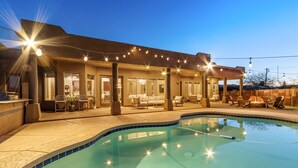 A modern outdoor pool area with a covered seating area and string lights.