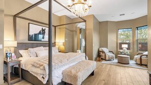 A four-poster bed with a fluffy white comforter, a chandelier, and a large mirror.