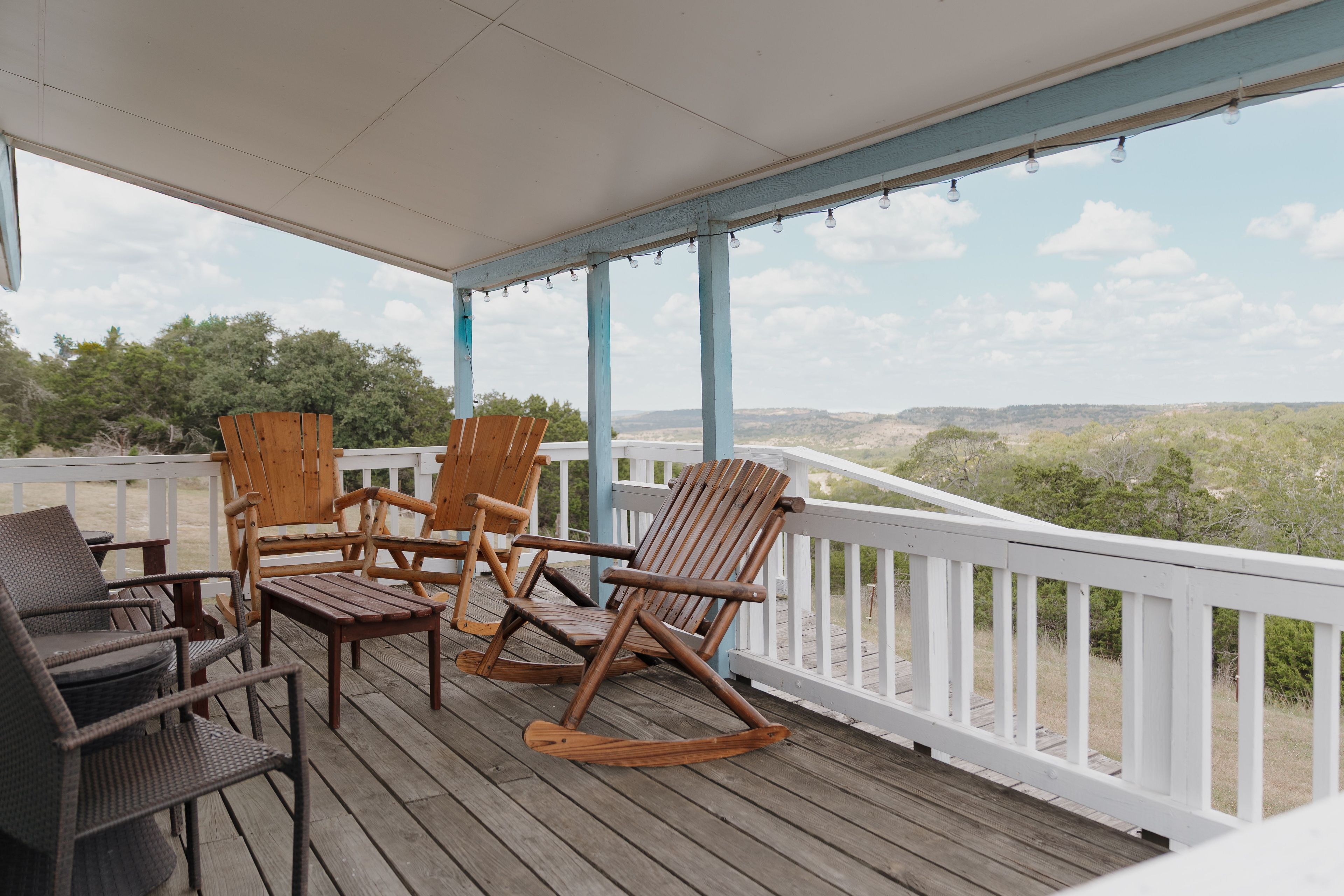Eine Holzterrasse mit Gartenmöbeln, darunter Stühle und ein Tisch, mit Blick auf eine Landschaft aus Bäumen und Hügeln.